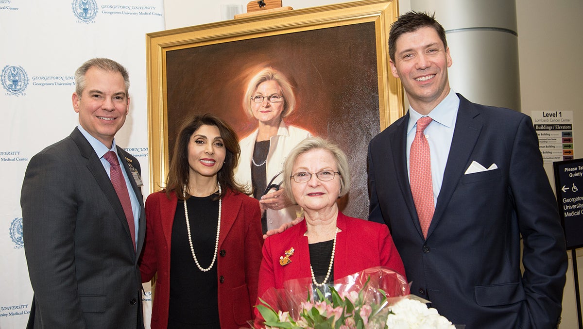 Four people stand together in front of a portrait