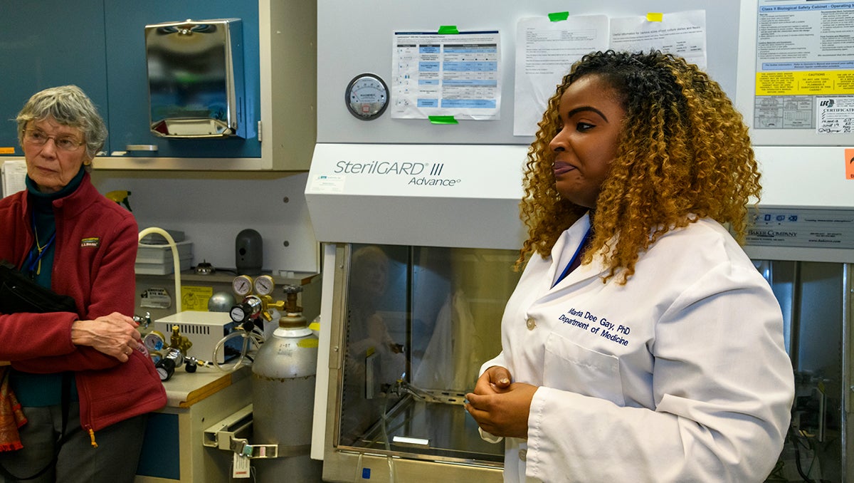 A woman in white lab coat speaks, while another woman listens in the background