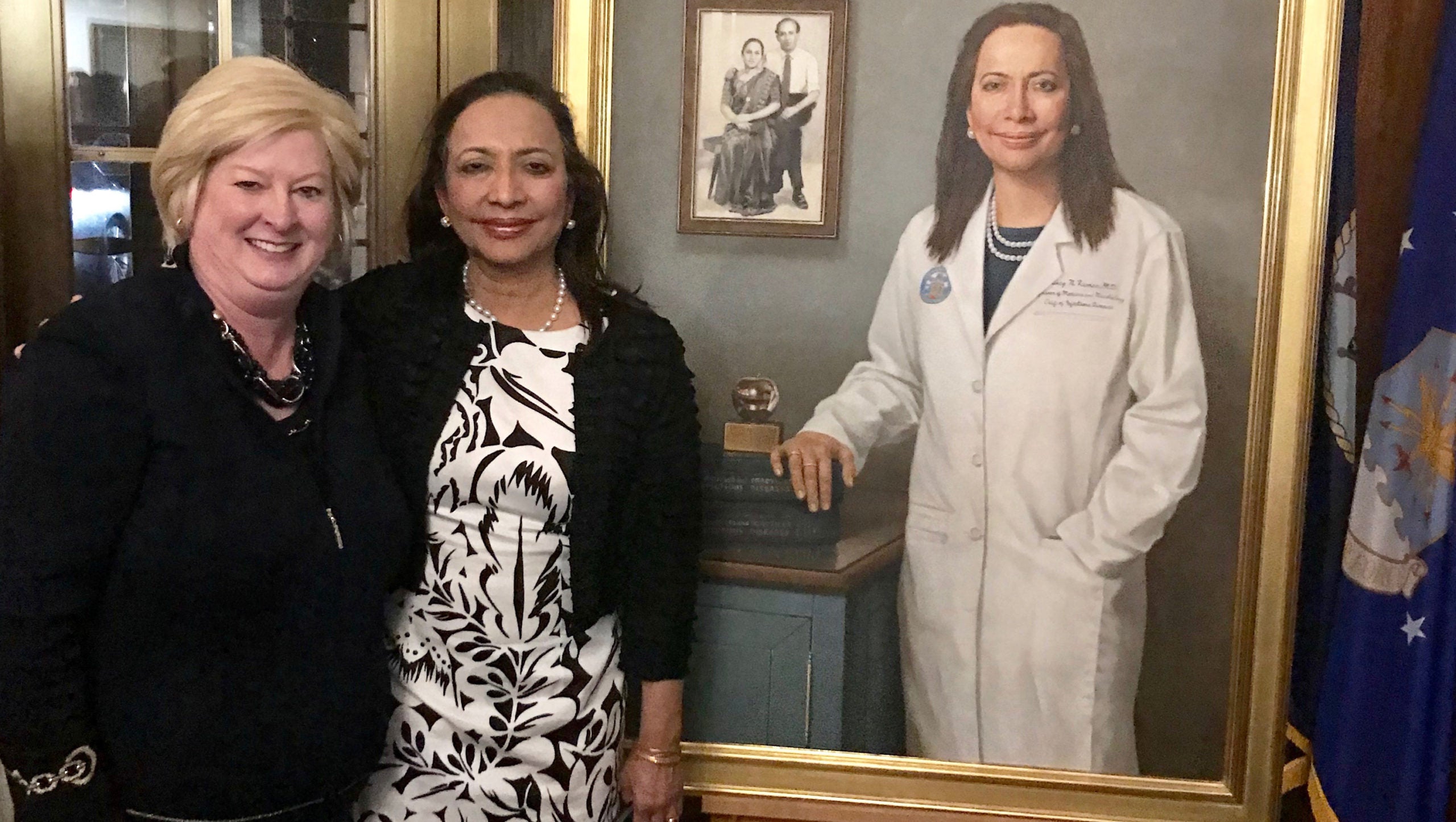 Two women stand side by side in front of a painting