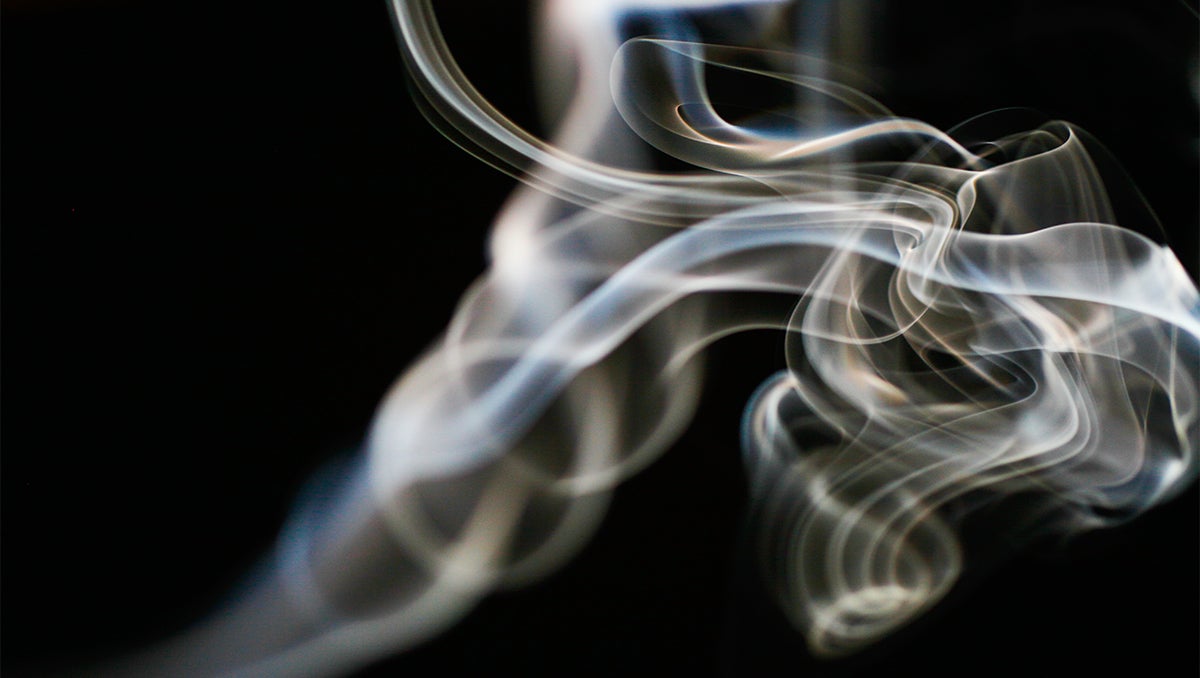 smoke from an unseen cigarette curls against a black background