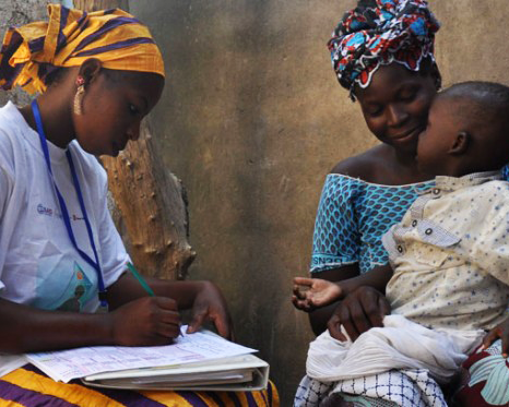 A woman writes out a health record as another woman holds a child on her lap