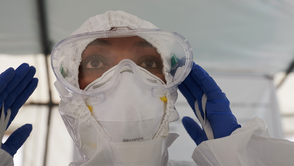 A woman dons protective goggles in addition to a mask and headcovering