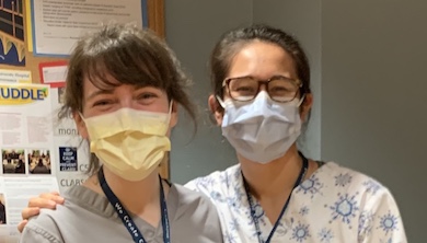 Two nurses stand side by side wearing protective masks