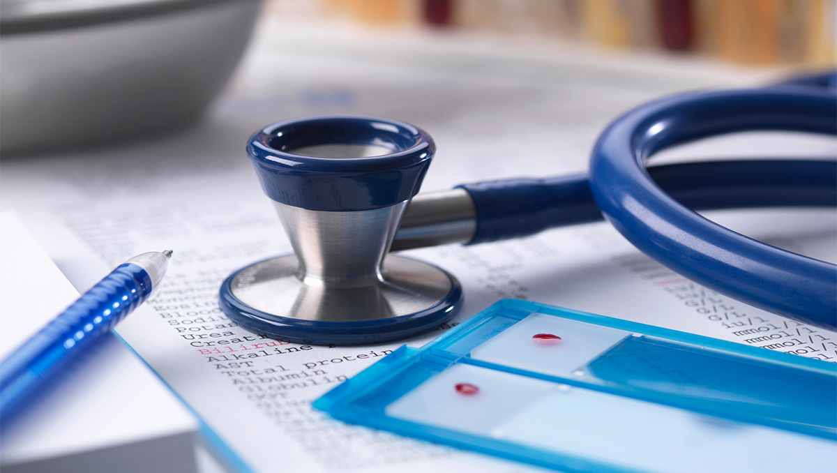 A stethescope lies on a table over a chart with a pen nearby