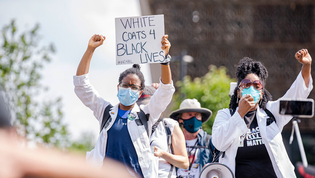 A group of medical students wearing white coats and surgical masks participate in the White Coats for Black Lives protest.