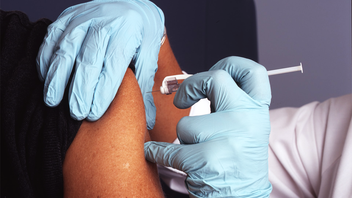 A nurse wearing blue gloves administers a vaccine (vaccination) into a male patient's arm