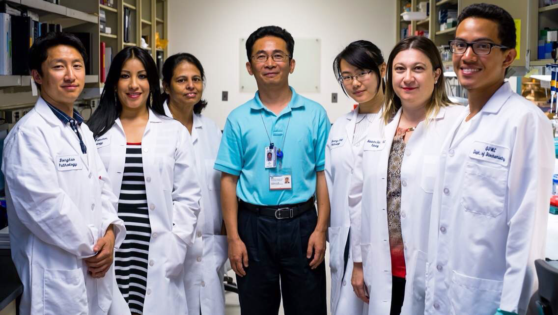 A group of people, most wearing white lab coats, stand together in a lab