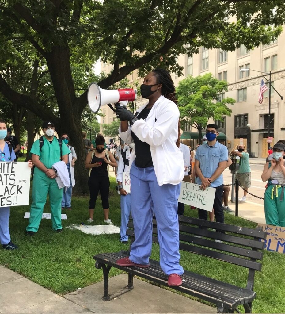 A person stands on a bench with a megaphone at a protest