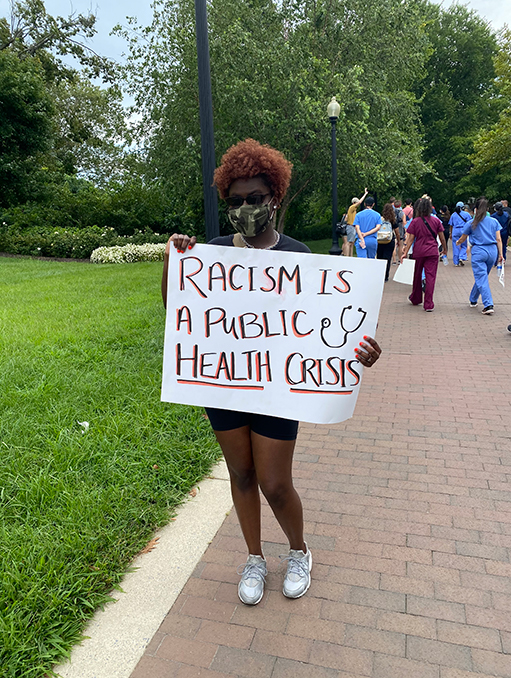 A student holding a sign that reads "Racism is a public health crisis"