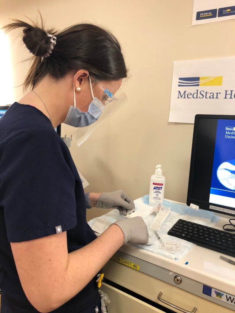 Elizabeth Douglas wears a mask and gloves to prepare a dose of the vaccine in a clinical setting