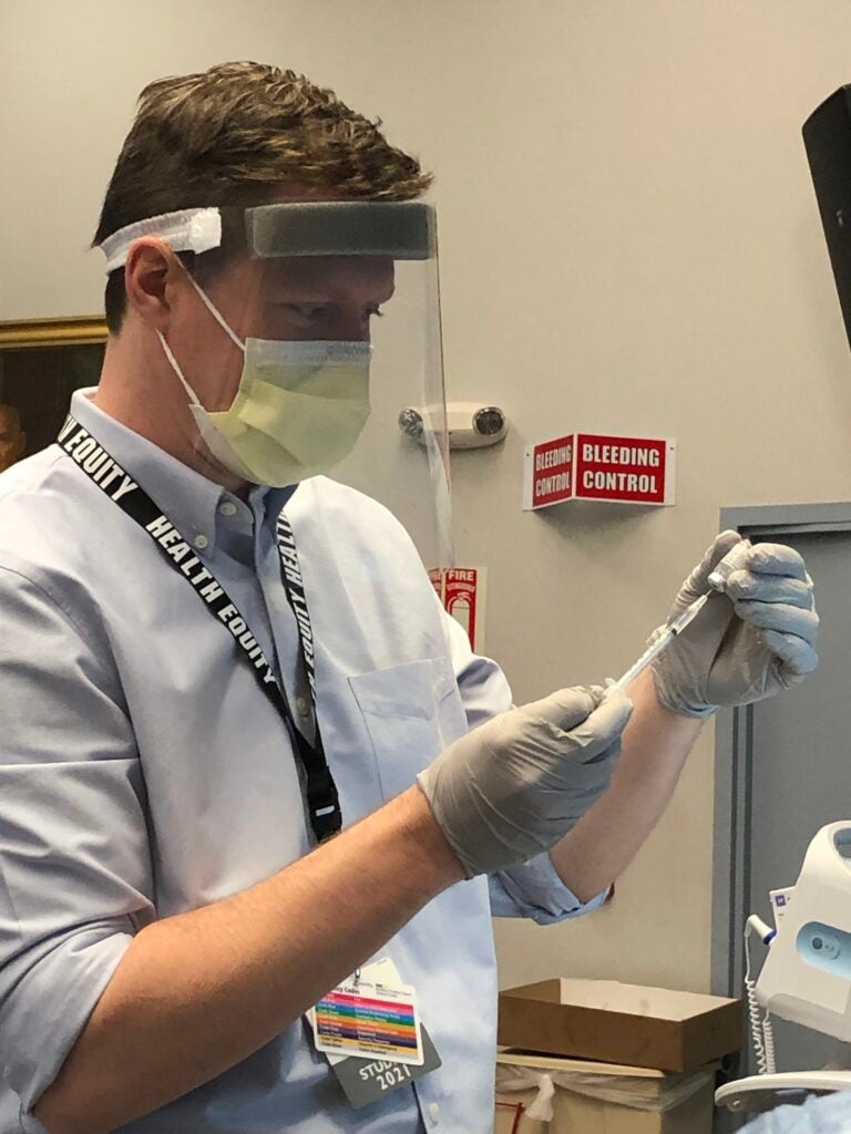 Stephen Kane wears a mask and gloves to prepare a dose of the vaccine in a clinical setting