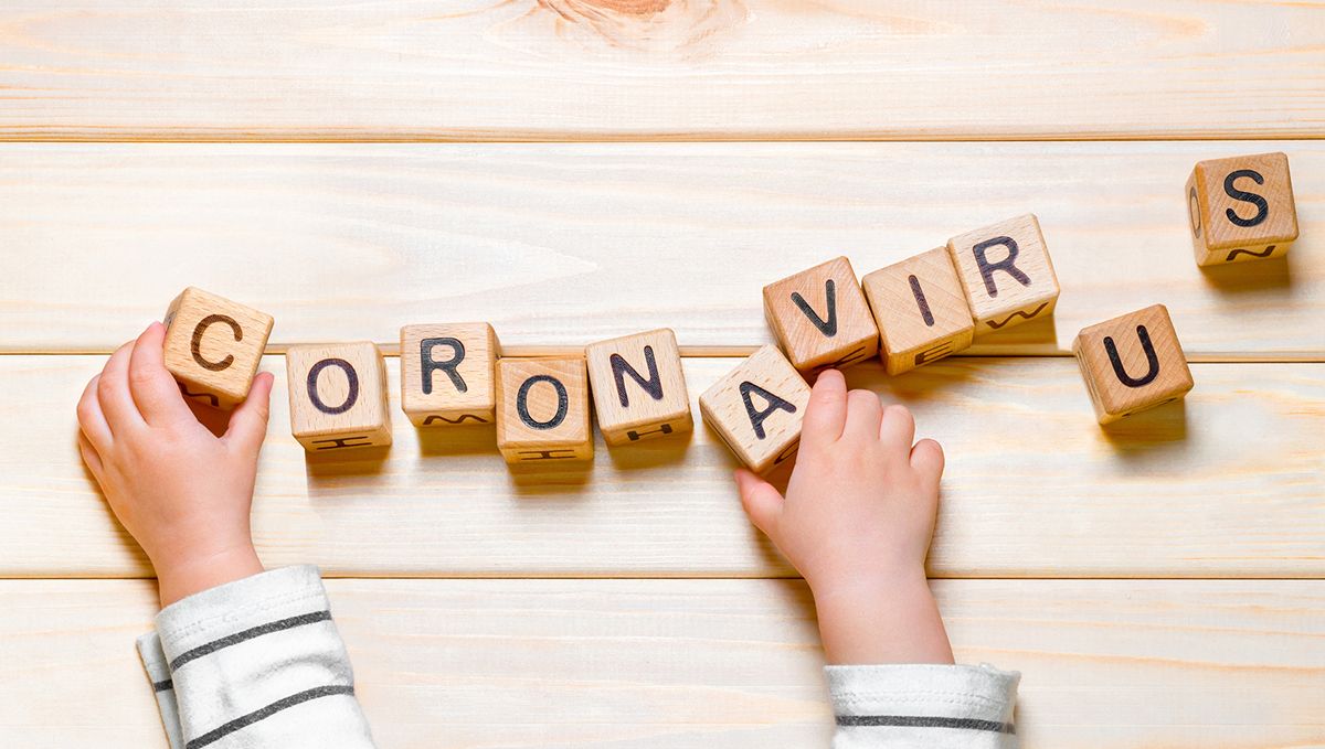 A child's hands play with letter blocks that spell out the word coronavirus