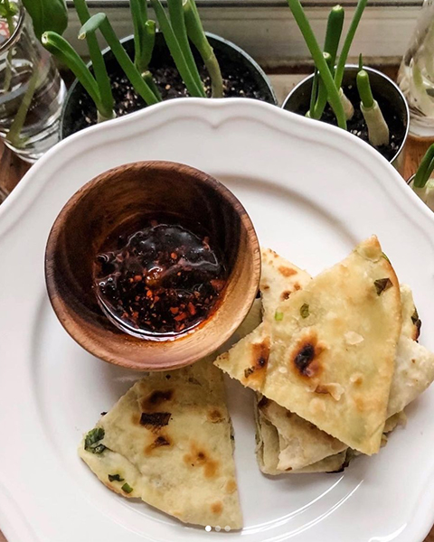 A white plate with quarters of scallion pancake and a small bowl of sauce