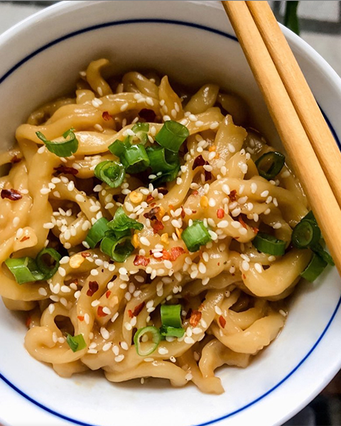 Sesame noodles in a bowl with chopsticks laid alongside