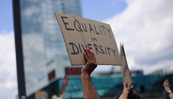 A hand holds a sign that reads Equality in Diversity