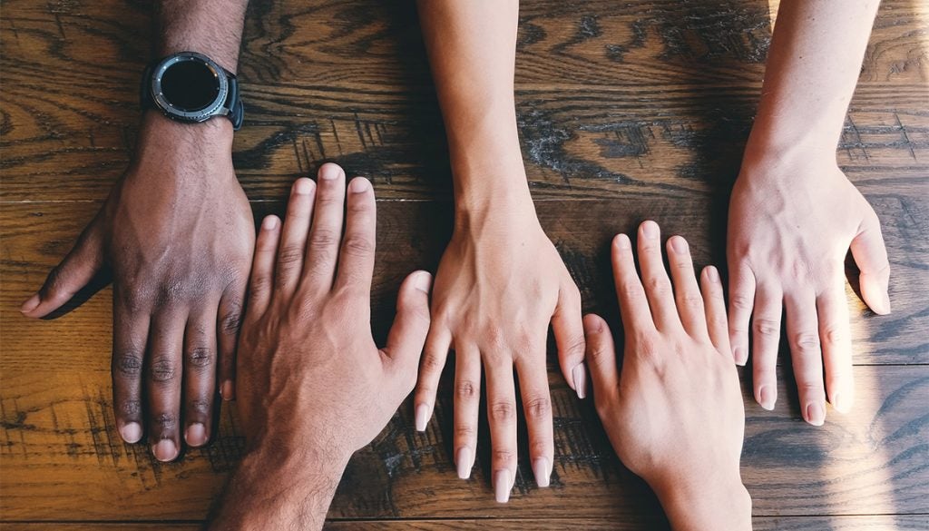 Five hands on a table of different skin tones