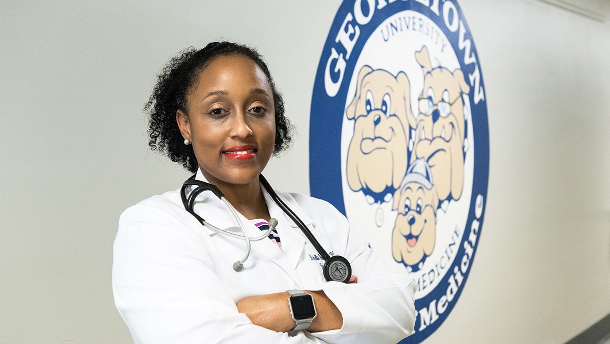 Dr. Michelle Roett stands in a hallway at GUSOM next to a mural of the Department of Family Medicine logo