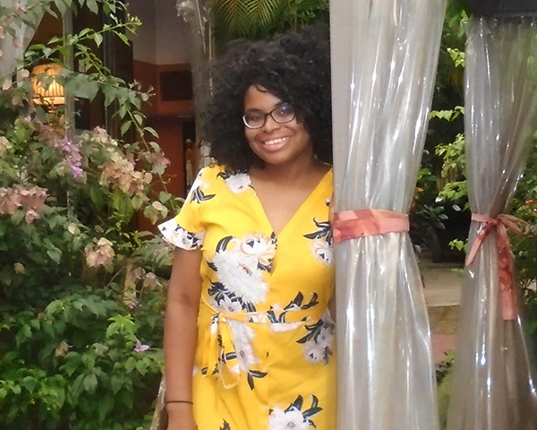 Jasmine Rogers stands surrounded by flowers in an outdoor seating area