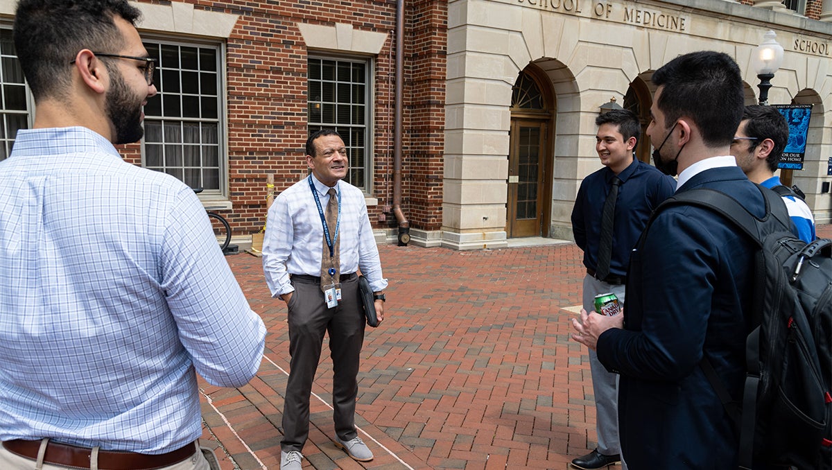 Lee Jones speaks with three medical students outdoors on campus