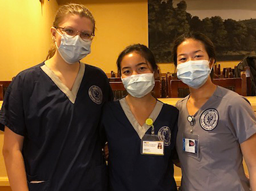 Three individuals in protective medical garb stand together