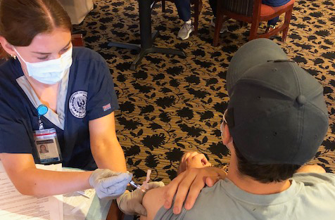 A nurse administers a shot to a person wearing a baseball cap