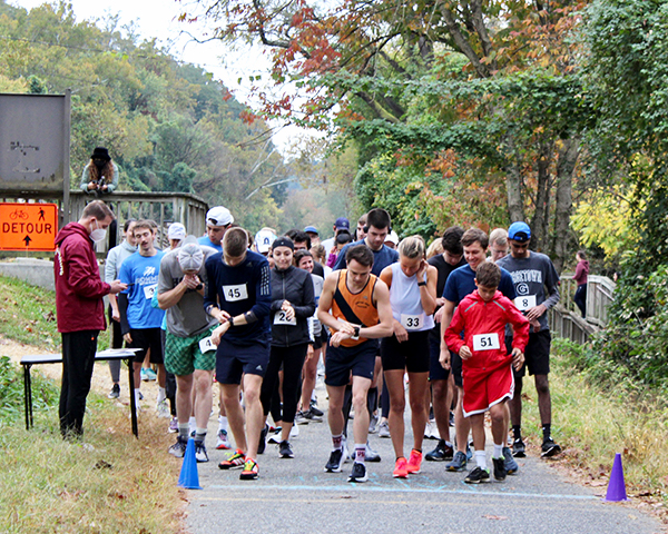 A large group of runners gets ready to start on a paved path in a park setting