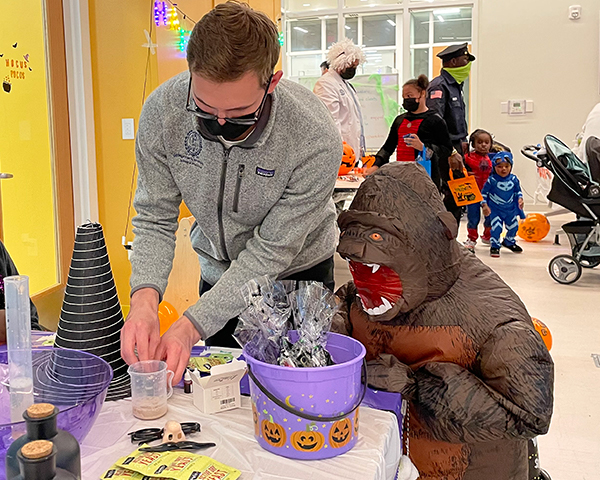 A young man assists a child in monster costume with a craft