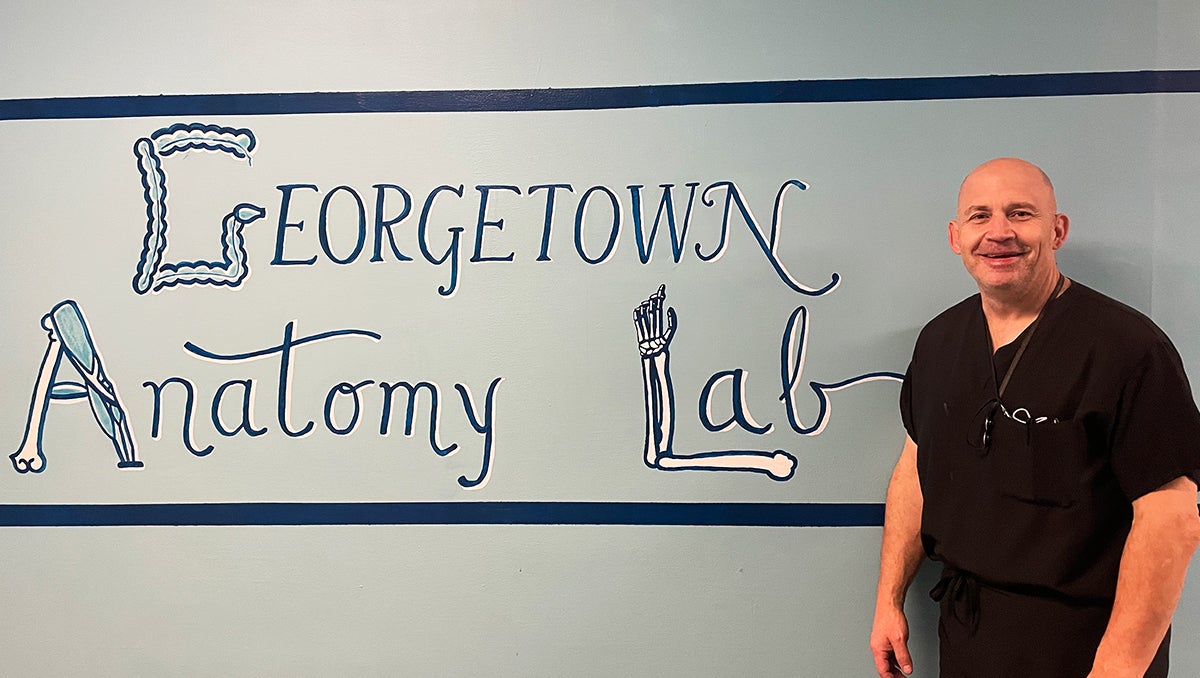 Mark Zavoyna stands in front of a hallway mural that says 