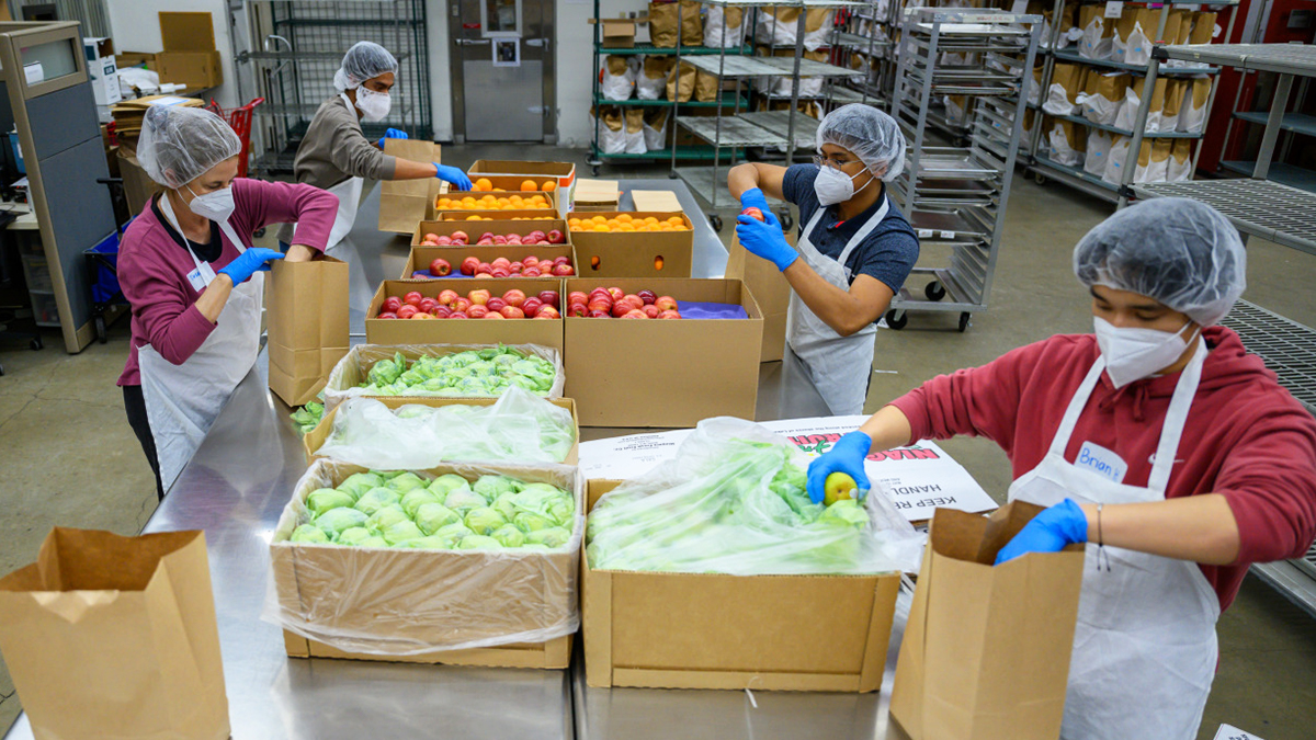 Several people stand at a table sorting produce into bags