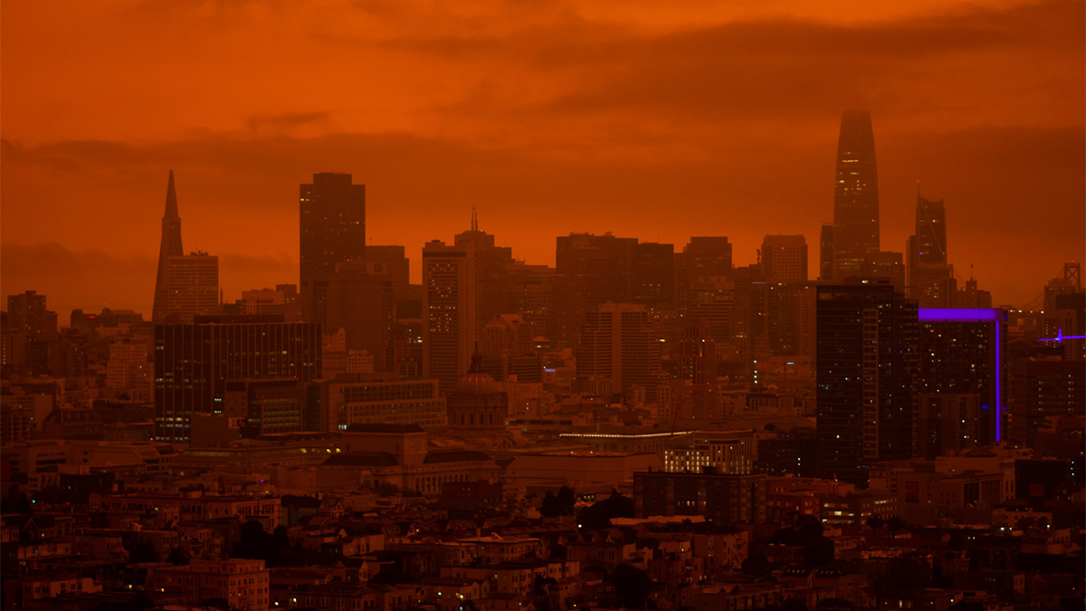 The San Francisco skyline is shrouded in smoke and illuminated by a dull orange glow in the sky