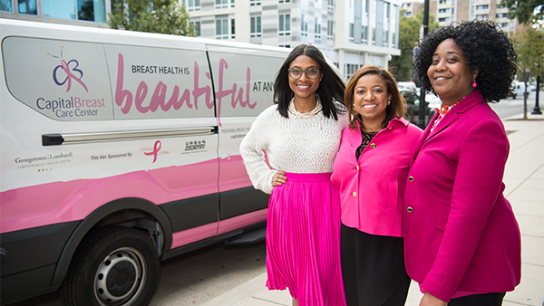 Three women stand with the van used by the Capital Breast Care Center for outreach activities