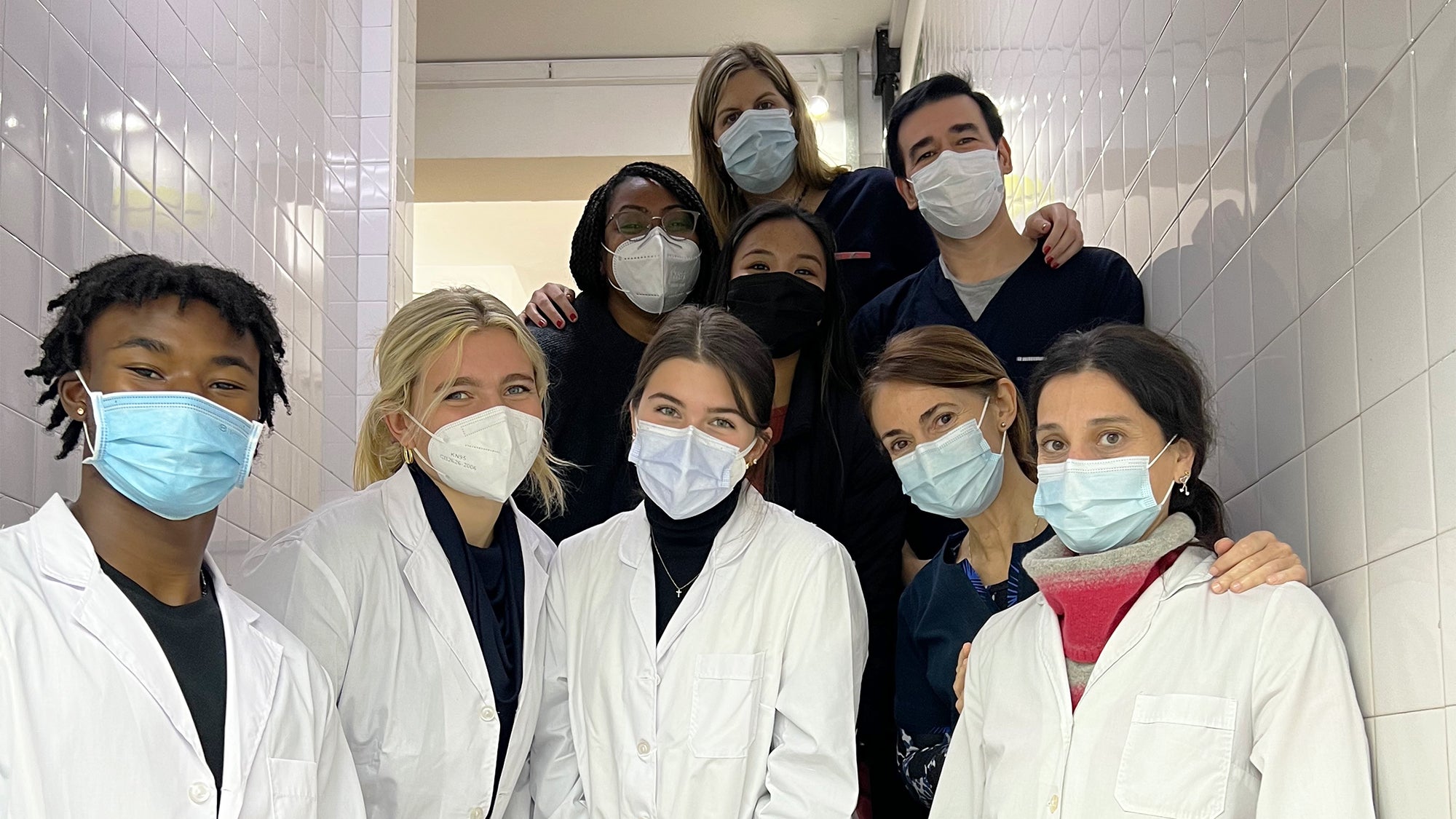 Students wearing white coats and masks stand together in a hospital hallway