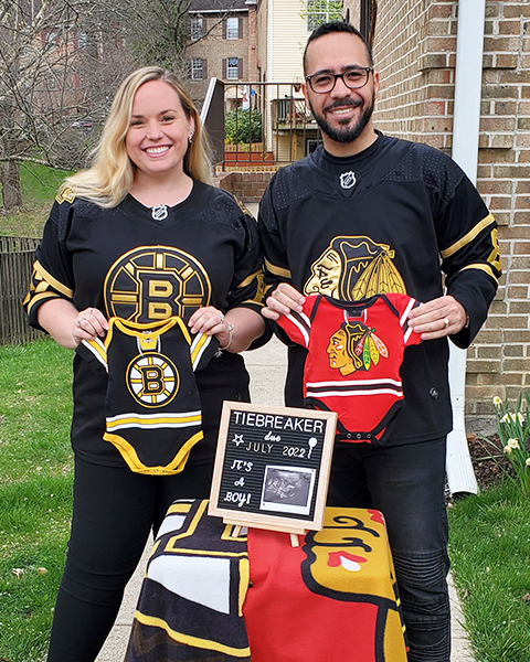 Mohamed Elsherief and his wife stand next to each other holding baby onesies for their respective NHL teams for a gender reveal for their baby