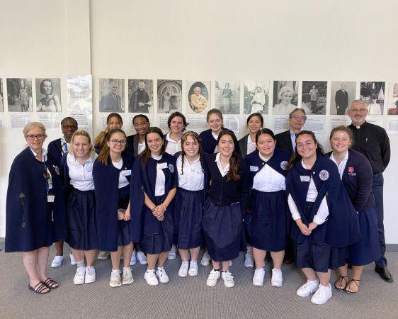 A group of people stand together, most dressed in a traditional nurse's uniform