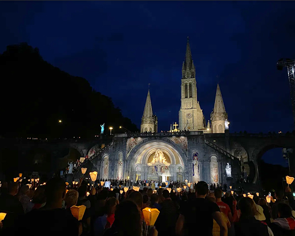 A torchlights parade of crowds of people with the cathedral lit up against the evening sky