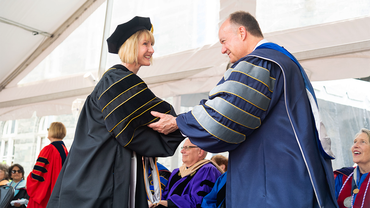 A PhD student in academic regalia accepts her degree from President DeGioia at commencement