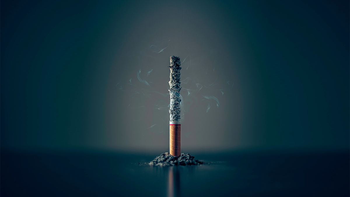 A cigarette almost burned to ashes sits upright on a surface