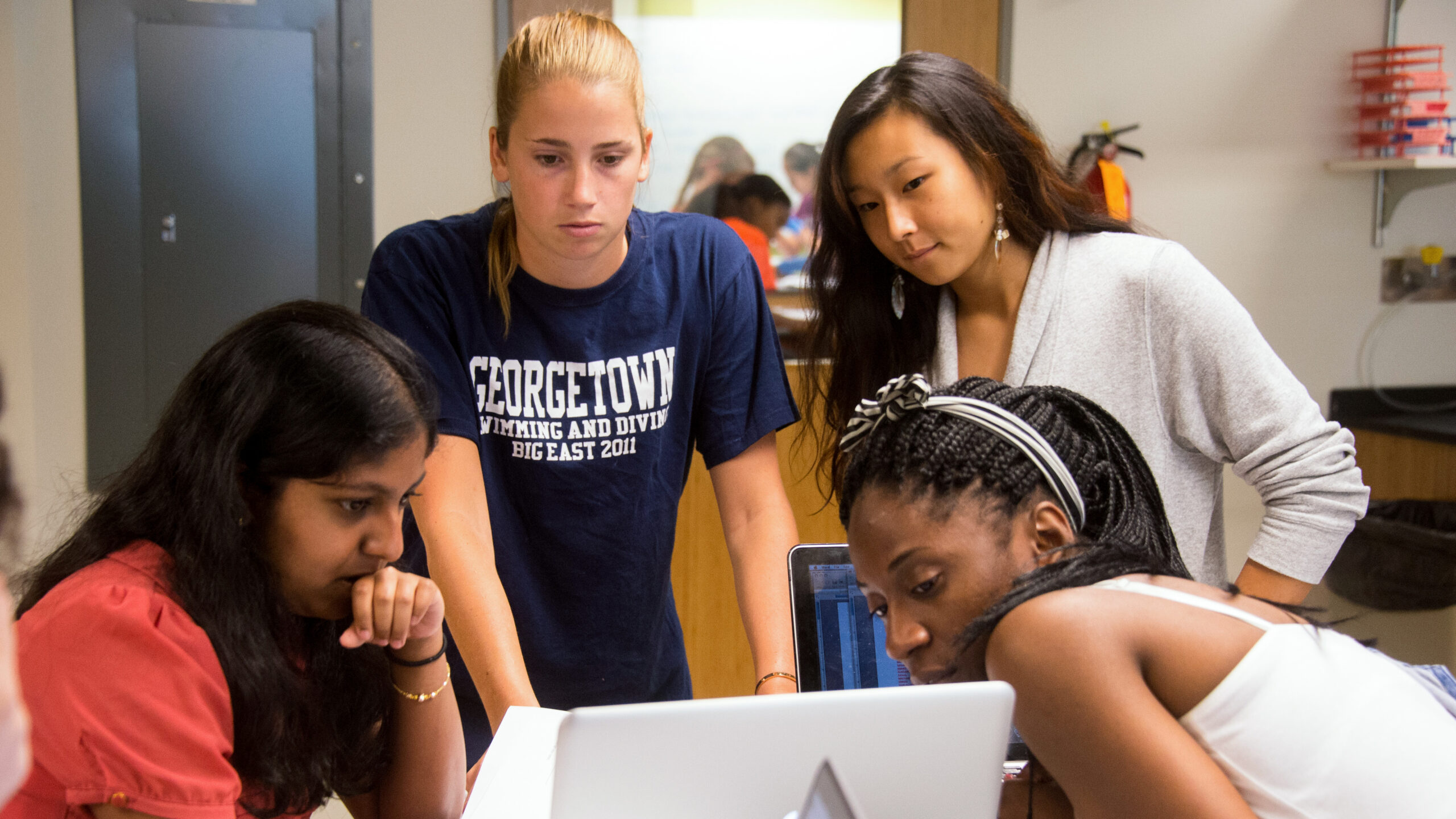 Four Georgetown College students look at the display of a laptop