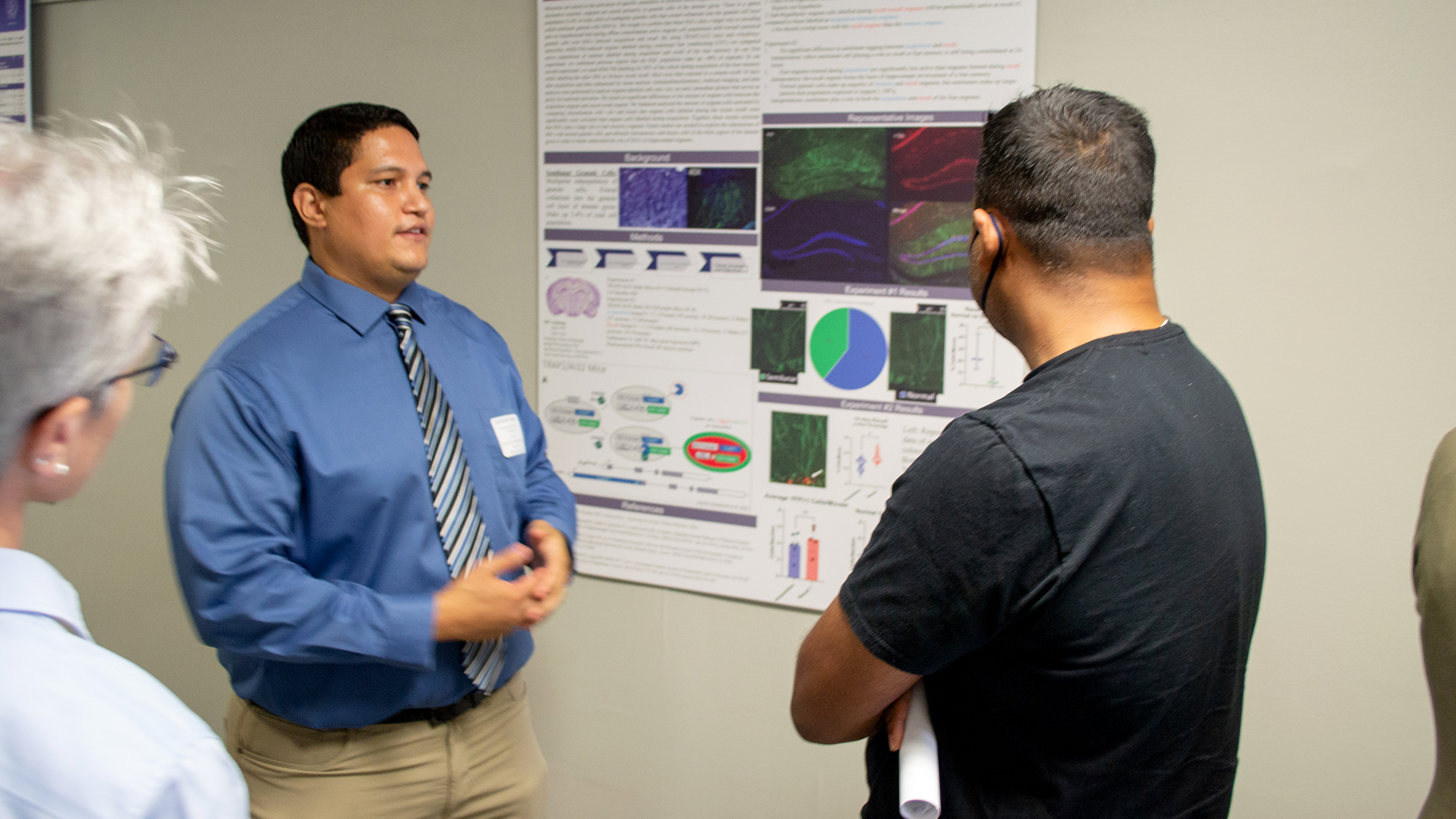 A student stands in front of his poster talking to two other people