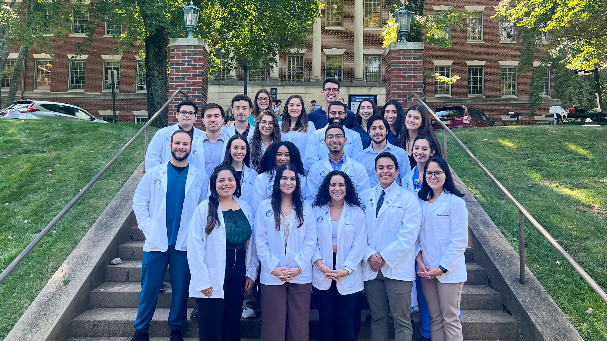 A group of medical students stands on the steps in front of the Med-Dent Building on campus