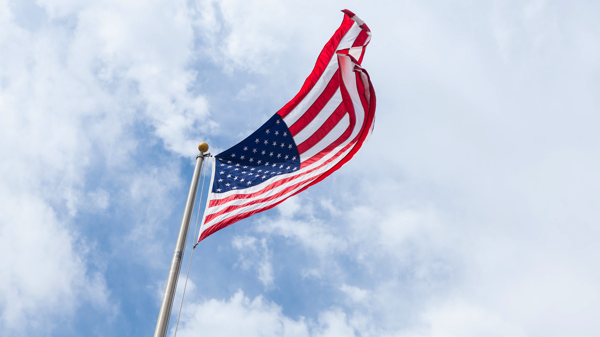 An American flag on a flagpole viewed from the ground against a partly sunny sky