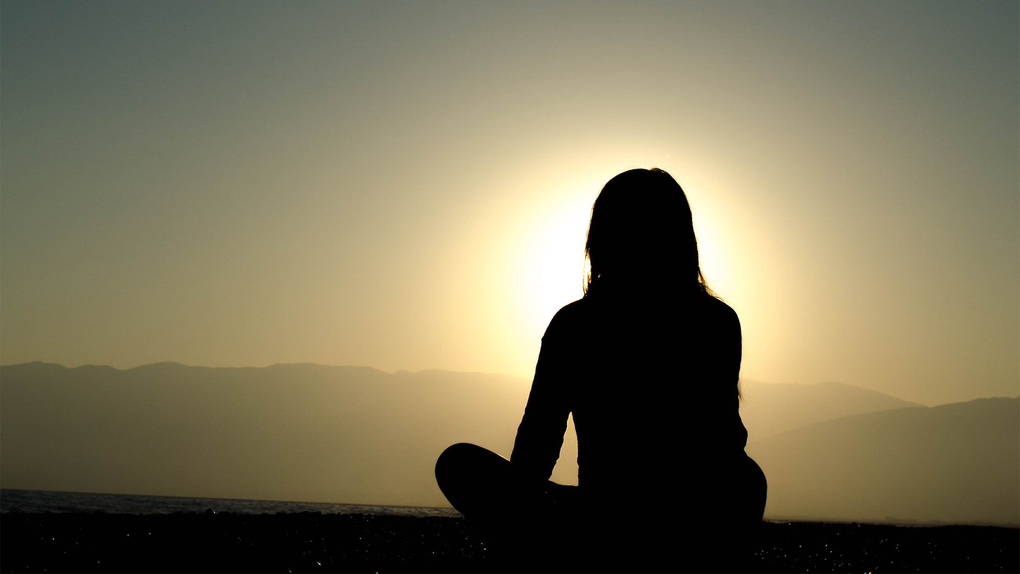 A seated female figure contemplates the sunrise
