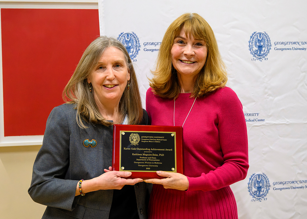 Karen Anderson and Kathy Maquire Zeiss stand next to each other, each holding a corner of an awards plaque