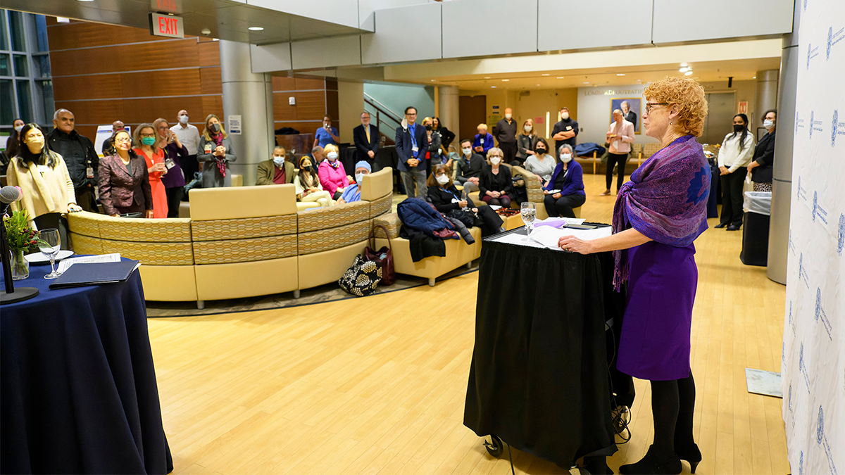 Eileen Moore speaks from behind a podium to a large room full of people