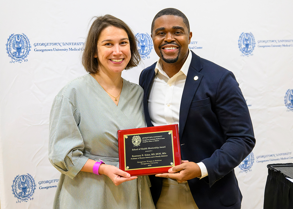 Sara Achrati and Christopher King stand next to each other, each holding a corner of an awards plaque