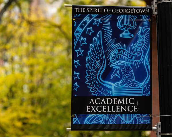 A banner reading "The Spirit of Georgetown: Academic Excellence" hangs from a pole on campus