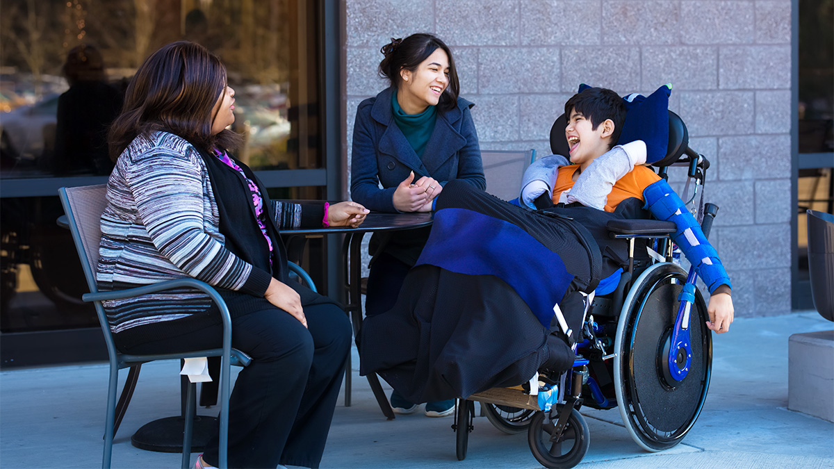 Two caregivers interact with a child with developmental disabilities using a wheelchair