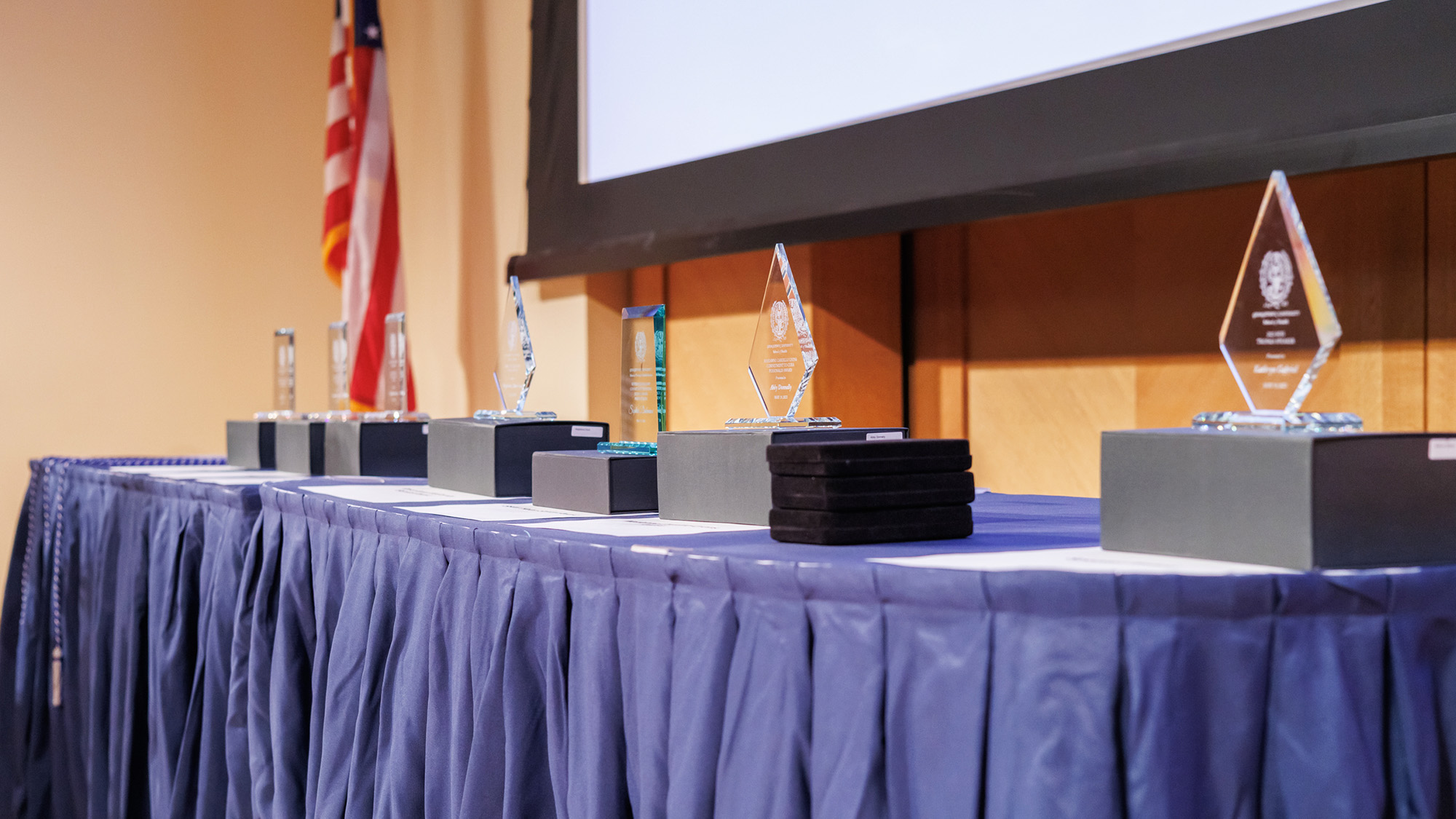 A table draped in blue tablecloth on which glass awards are arranged