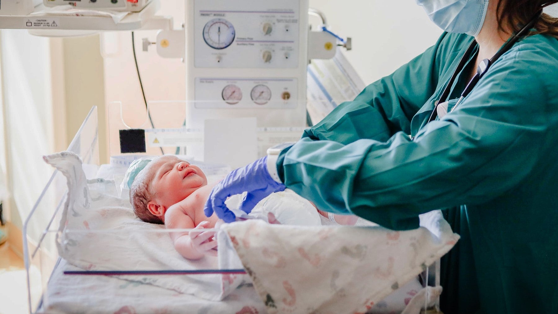 A nurse in scrubs tends to a newborn baby in a hospital crib