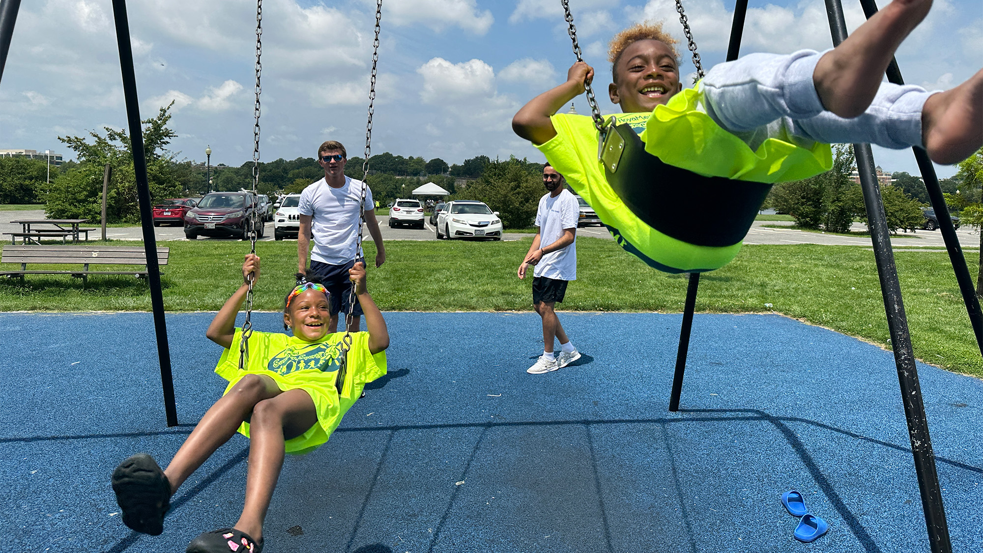 Two medical students push two children on swings on a swingset during HOYA Summer Sports Camp